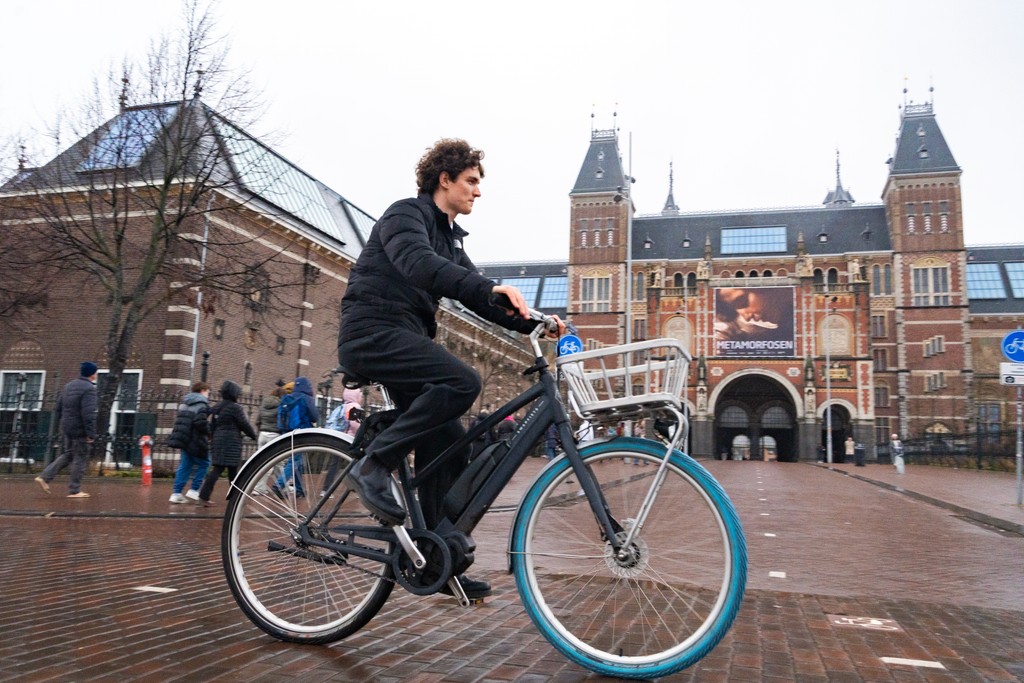 A person placing an e-bike battery into a charging locker, with charging cables connected and a digital display visible on the locker unit.