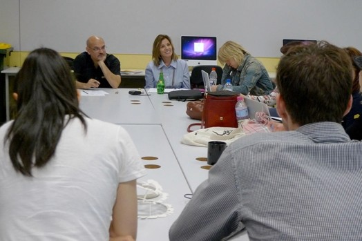 A photo of a group of people sitting at a conference table while working on laptops.