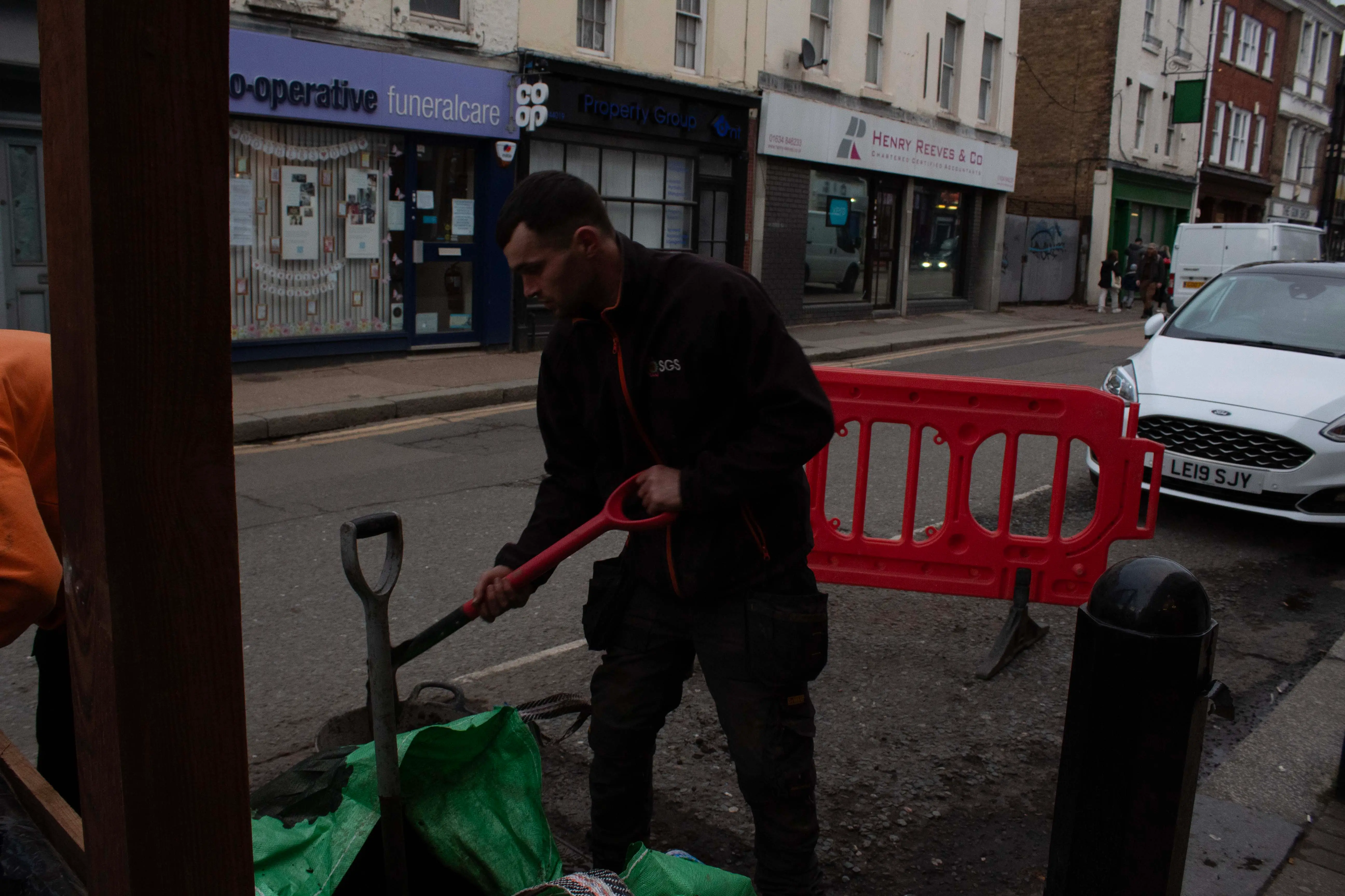 A person working on a green scooter near a street barrier in an urban setting.