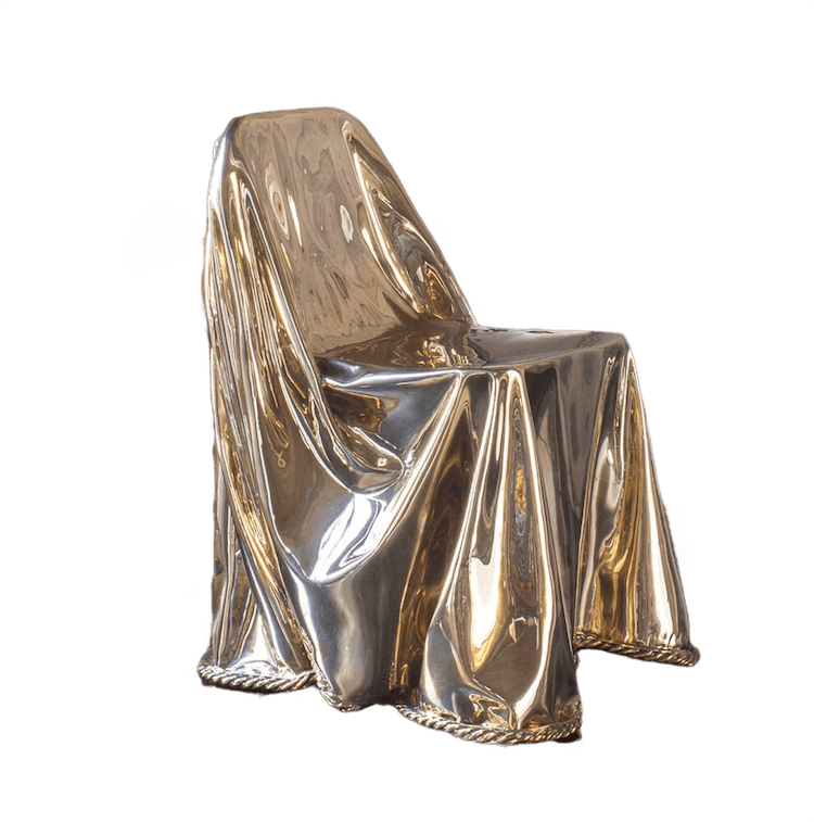 A chair draped in a reflective, gold-colored fabric. The fabric is sculpted to outline the chair's shape.
