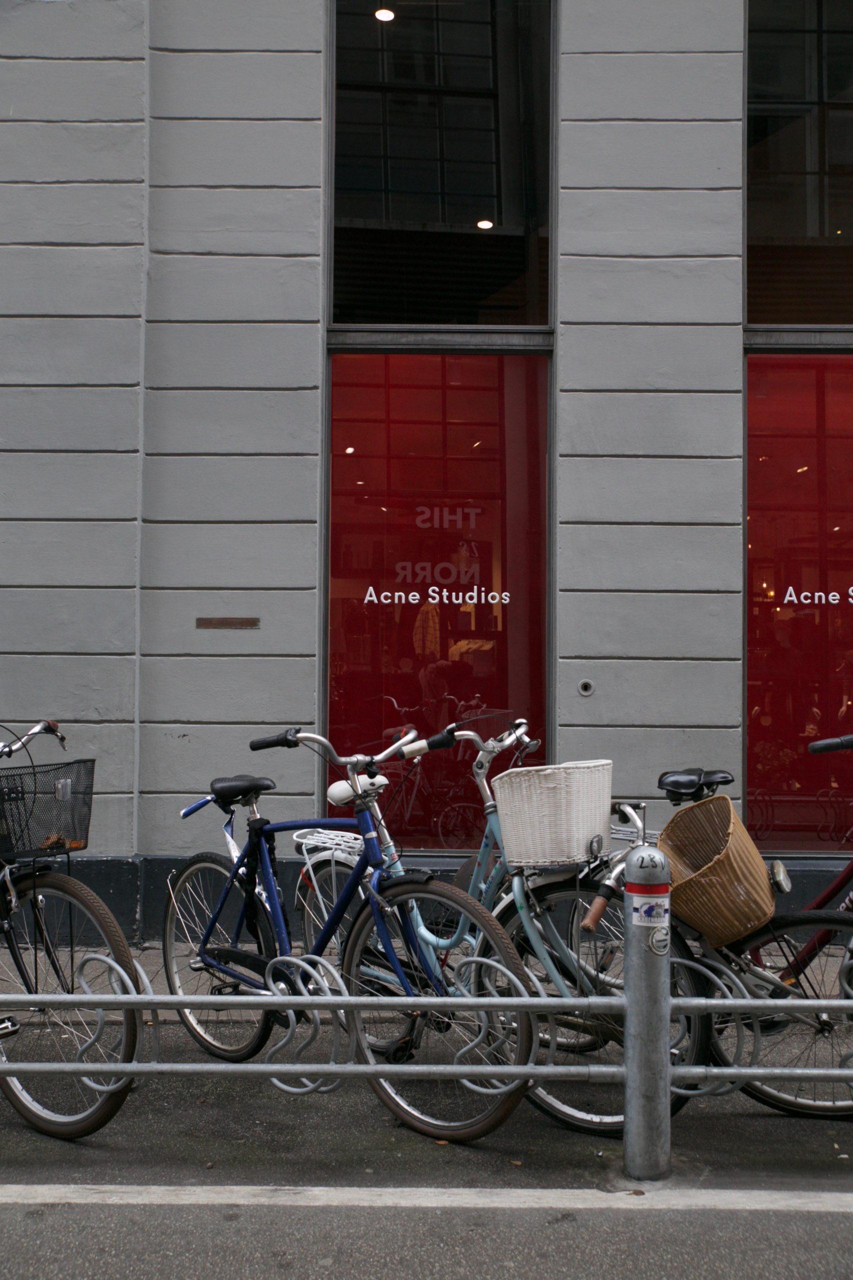 Bicycles parked outside an Acne Studios store with red-tinted glass windows