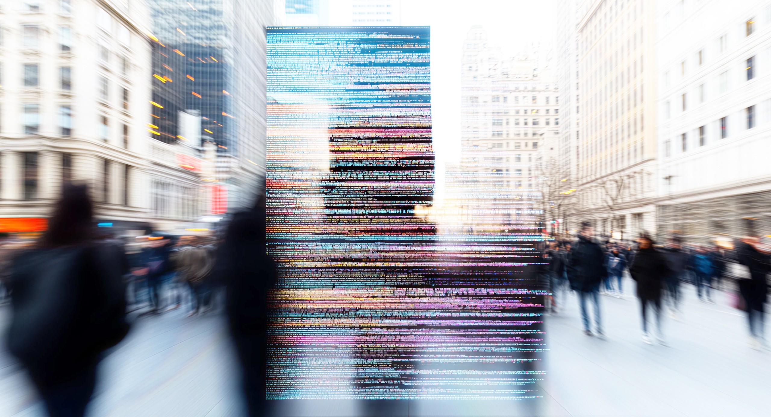 Blurred city street scene with pedestrians walking between tall buildings, overlaid with colorful lines of computer code in the center