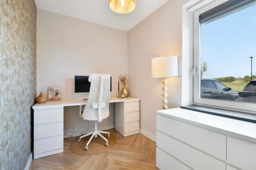 Een werkplek met een wit bureau, een bureaustoel en daglicht vanuit het raam.