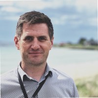 Minimalist profile shot of a man with long braids and a white shirt, set against a soft, light background.
