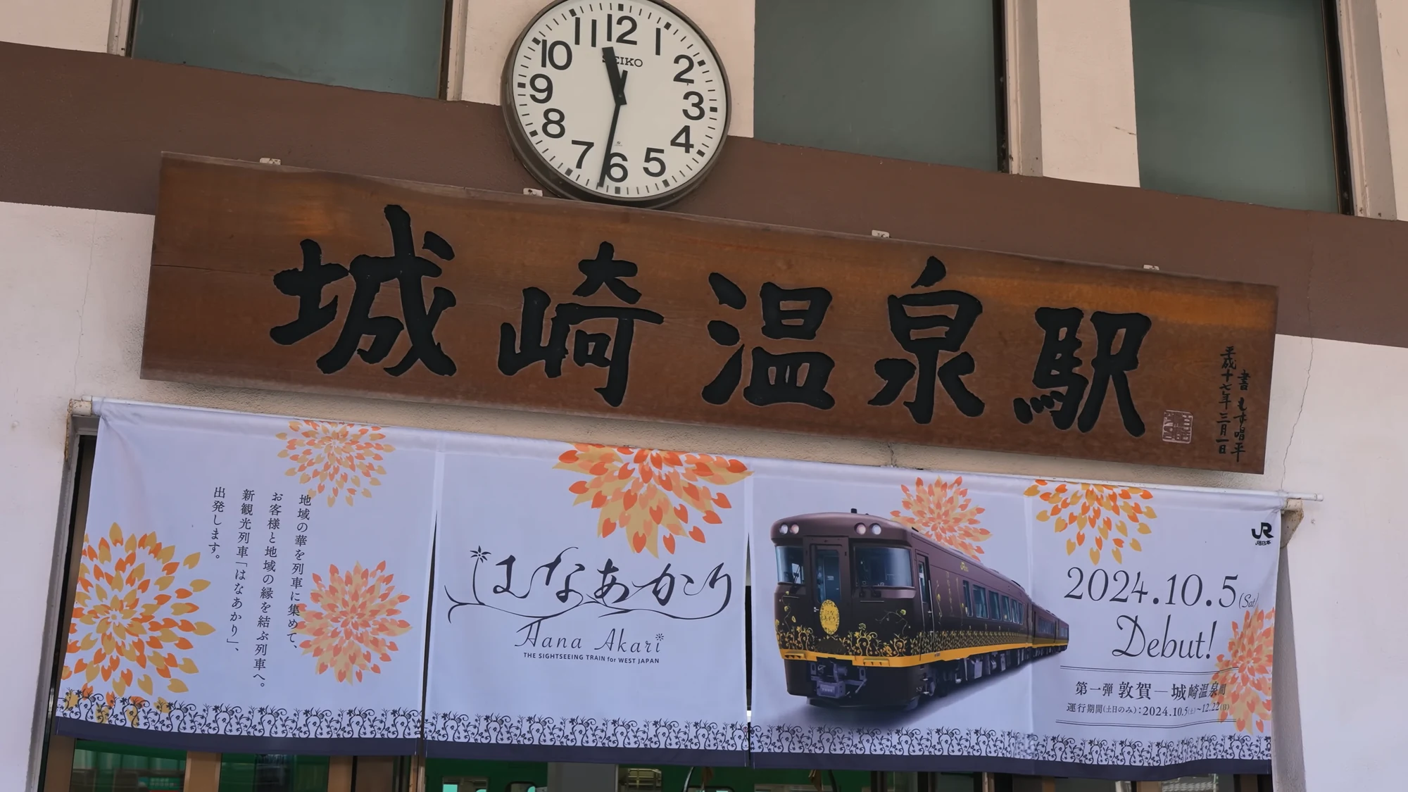 Carved wooden station sign reading Kinosaki Onsen beneath a platform clock.