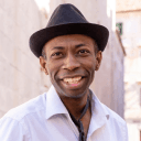 Man in fedora smiles at camera.