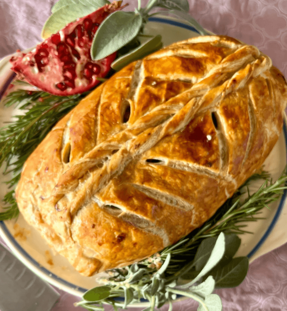 Baked mushroom Wellington with a golden pastry crust, garnished with herbs and pomegranate.