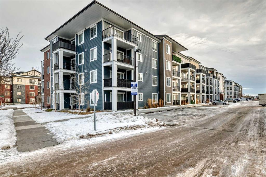 Four-story modern condominium complex featuring blue and brown siding, white structural columns, private balconies, and snow-lined streets in Legacy, SE Calgary