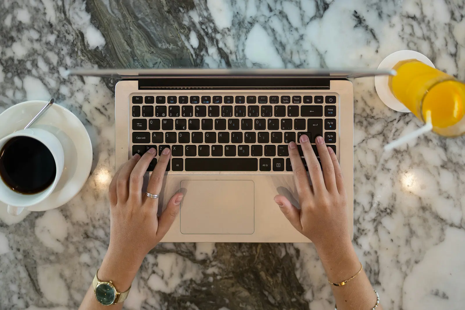 Hands typing on a laptop at a marble table with coffee and juice, symbolizing drafting a clear, organized demand letter.