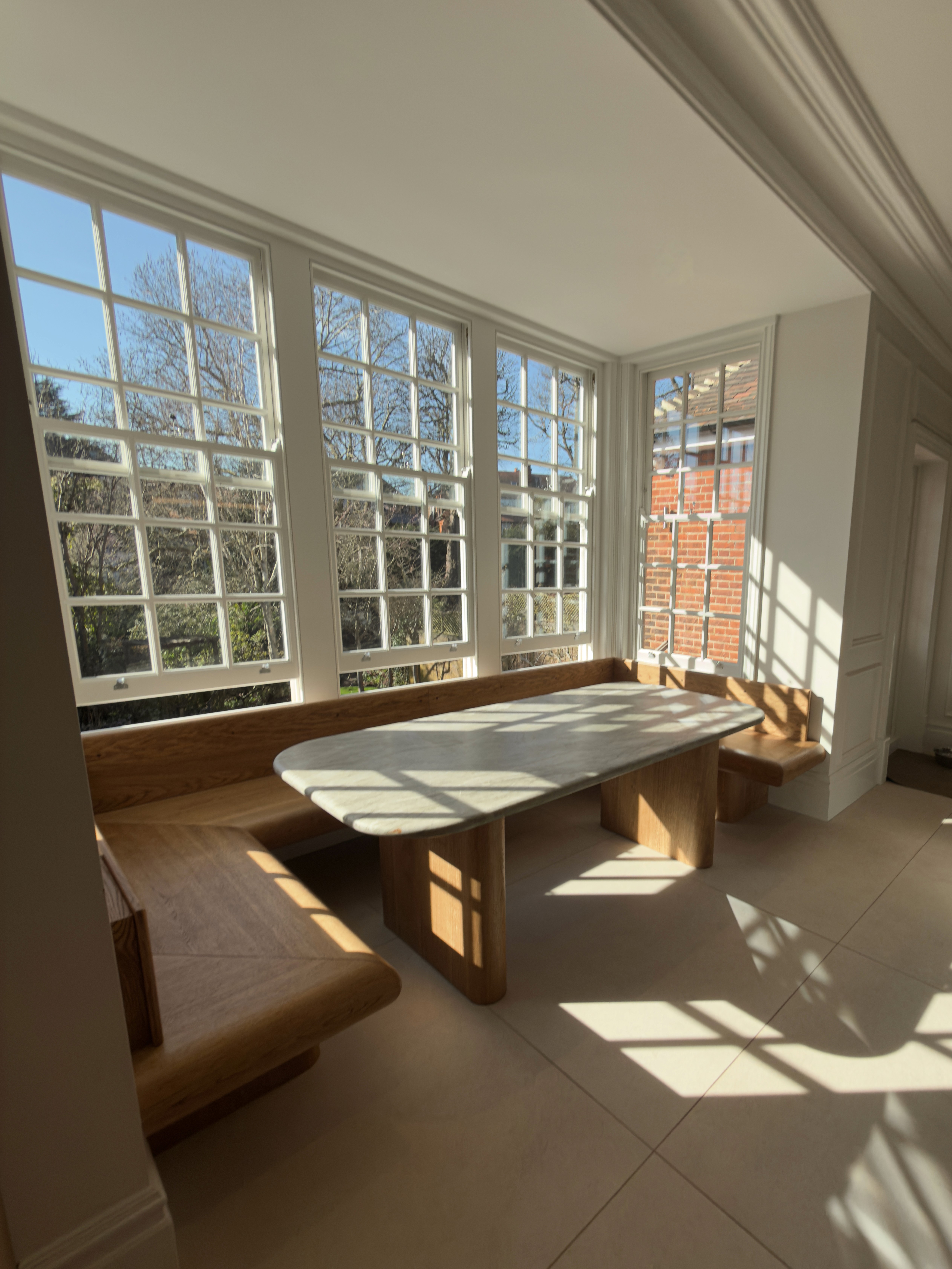 Sunlit dining space with timber & stone table and large traditional windows