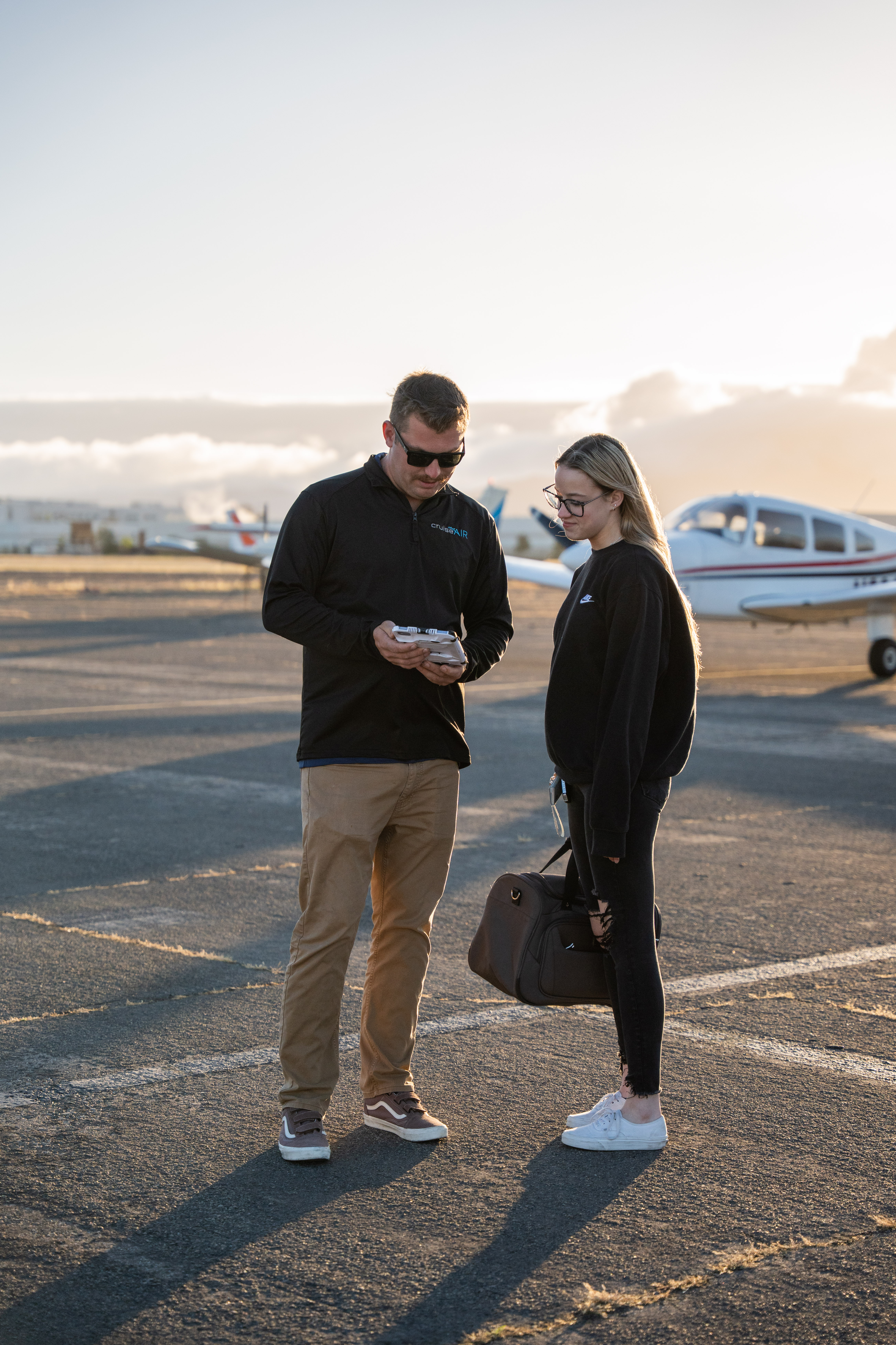 A smiling man with a beard wearing a dark green shirt, sitting at a table with a notebook, coffee cup, and laptop. He gestures with one hand while speaking, with a colorful abstract artwork framed behind him.