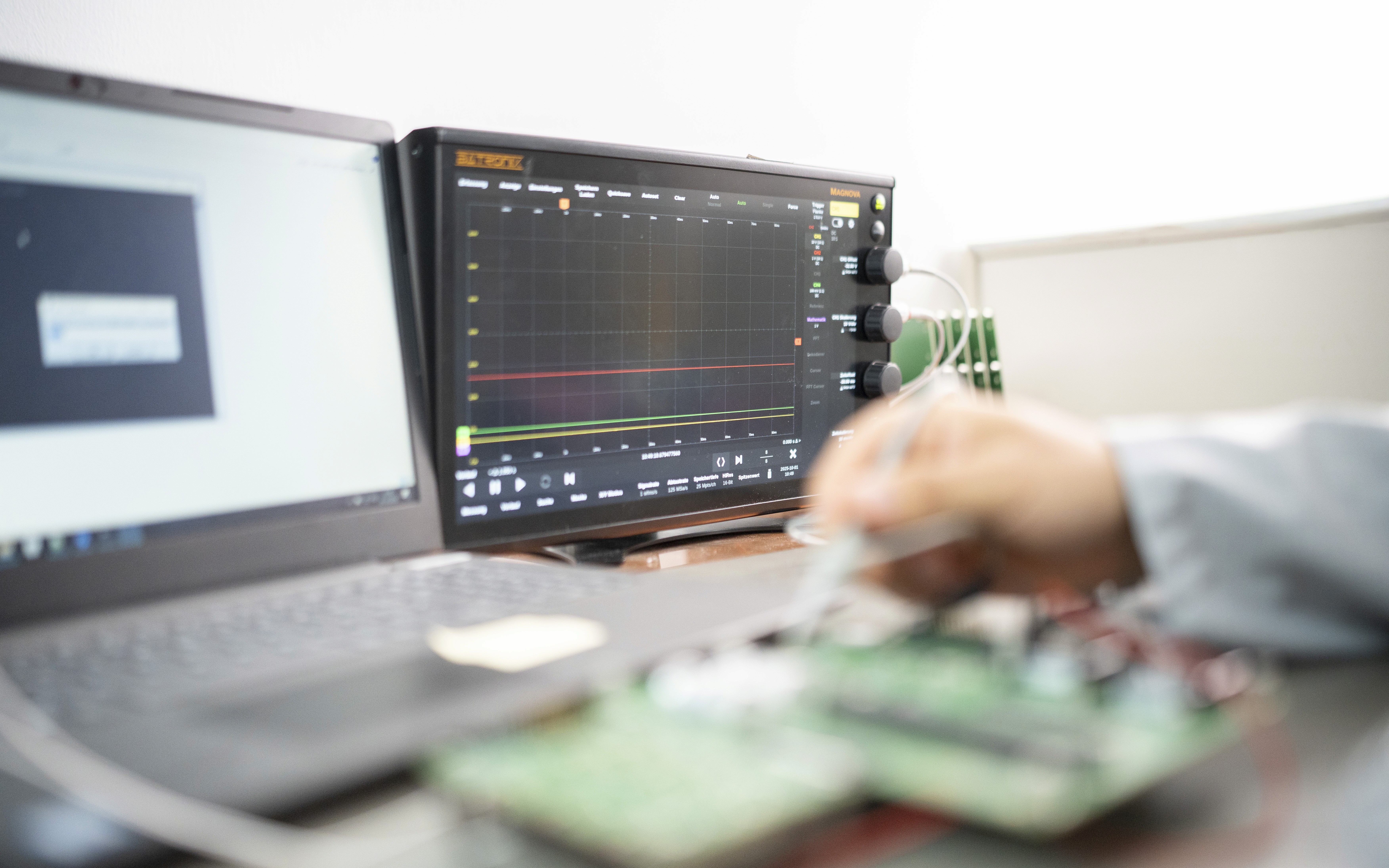 A man's hand carefully assembling a complex circuit board, with technical monitors displaying real-time measurements in the background.