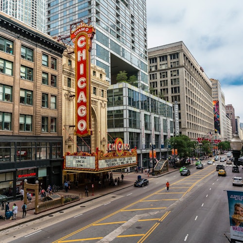 Chicago Theatre with its iconic marquee and sign on a busy city street, flanked by tall buildings and cars.