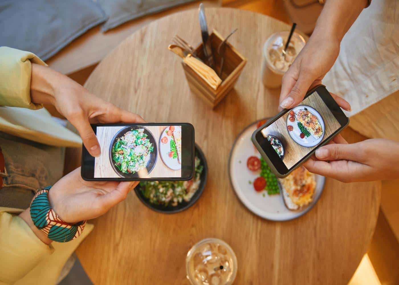 Two people with meals in front of them taking pictures with their individual phones