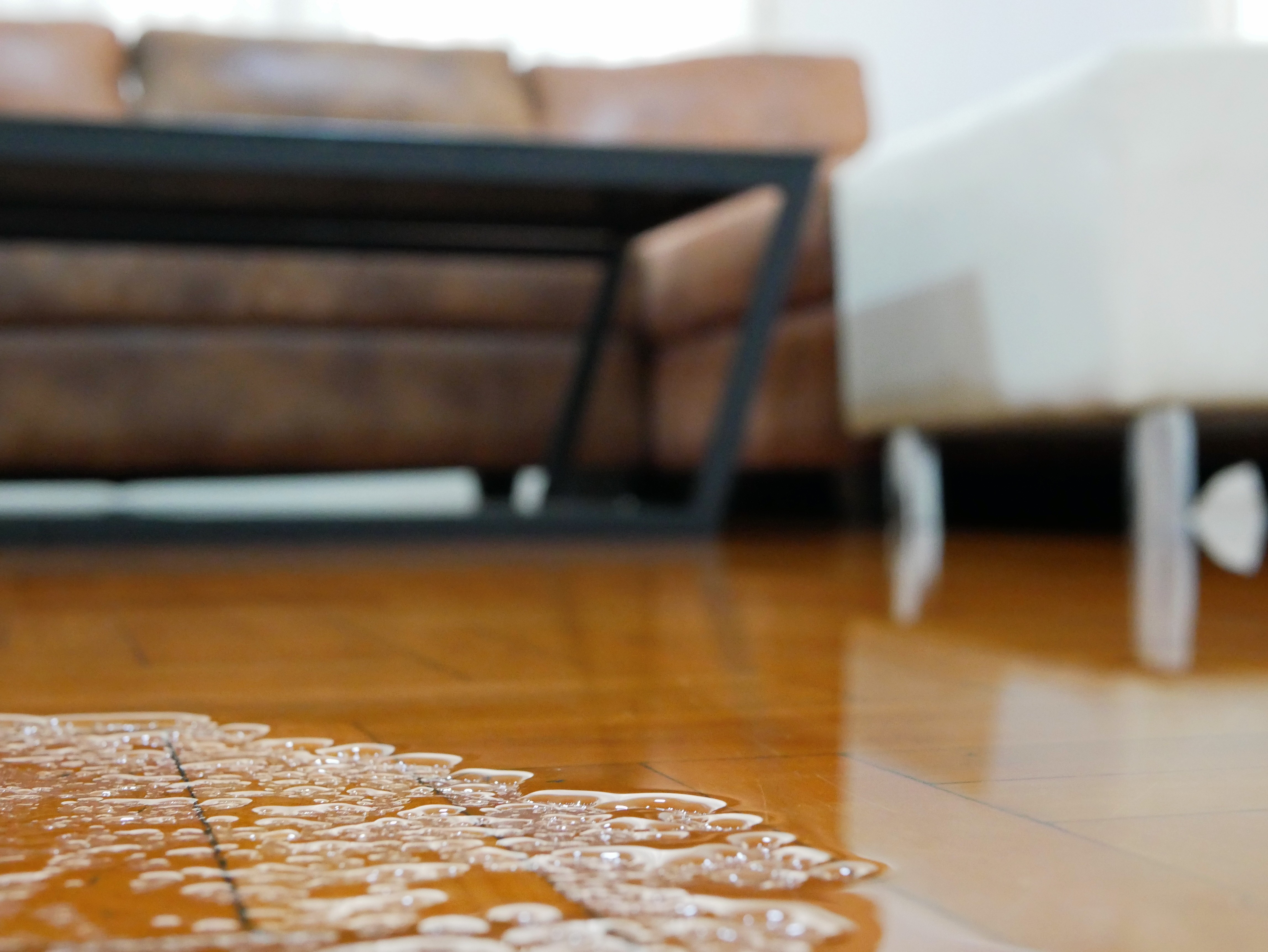 Standing water on hardwood floor inside a St. Louis living room, indicating water damage near furniture after a leak or flood