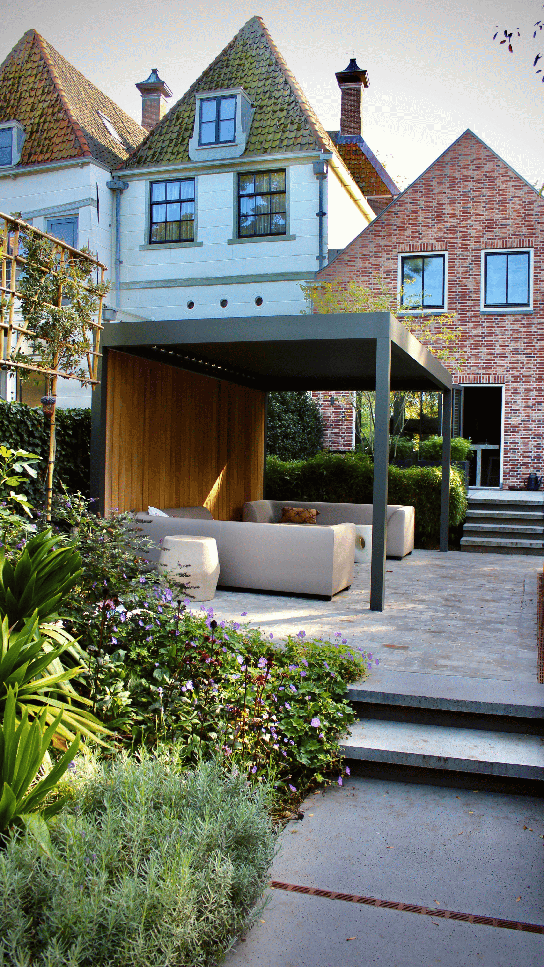 Modern living room with abstract art, beige sectional sofa, indoor plants, and large windows.