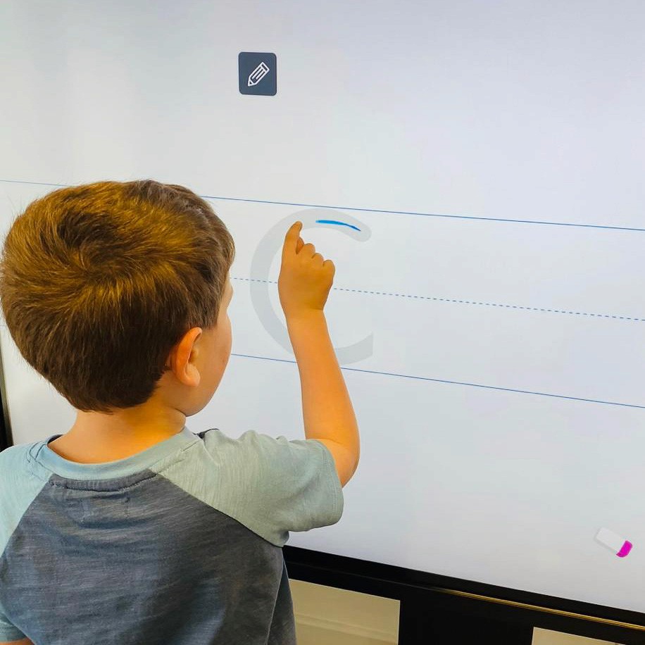 A child is using a digital whiteboard to trace letters from the alphabet. They're currently tracing the letter c.