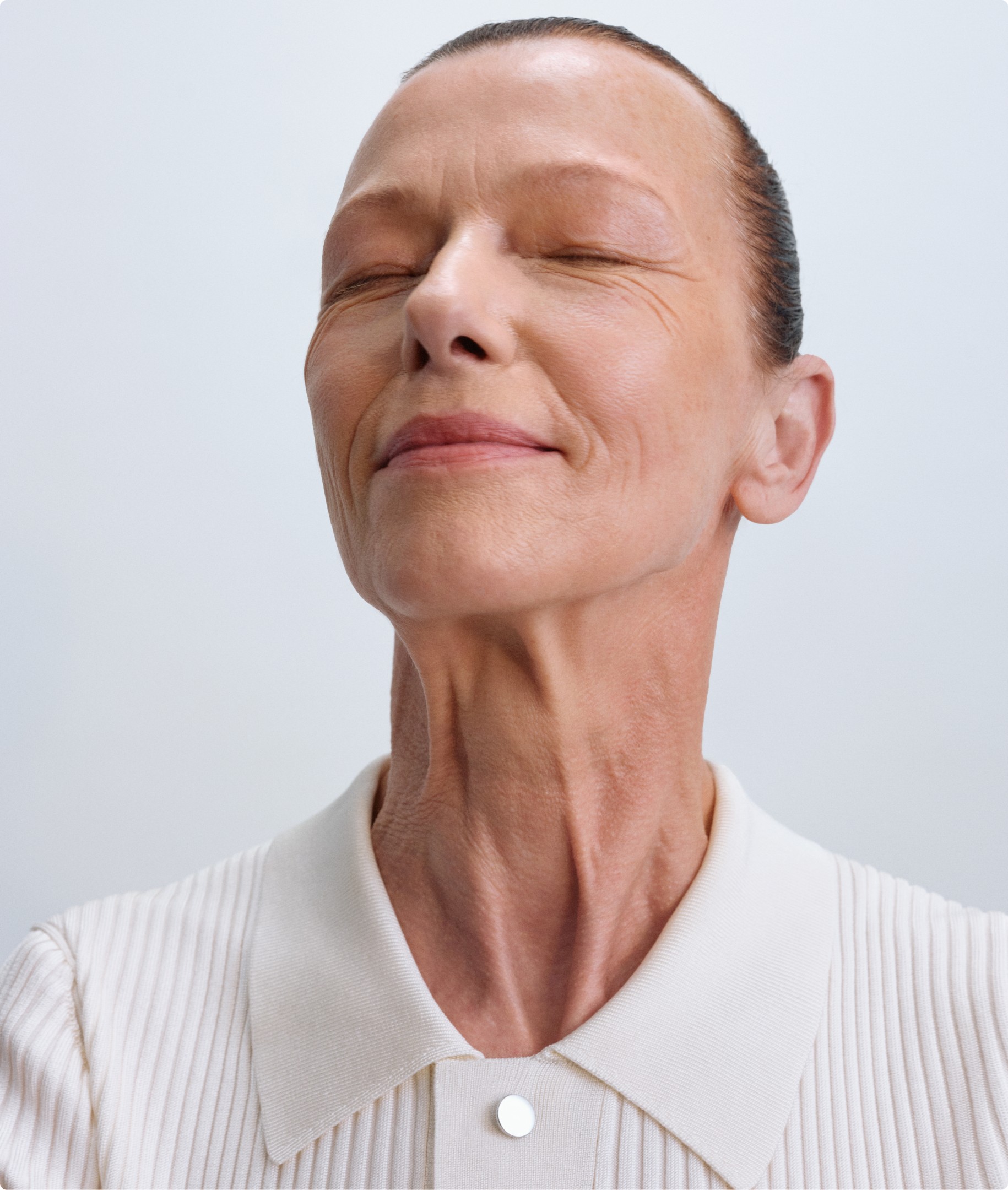 Portrait einer Person mit einem entspannten Gesichtsausdruck und geschlossenen Augen vor einem neutralen Hintergrund.