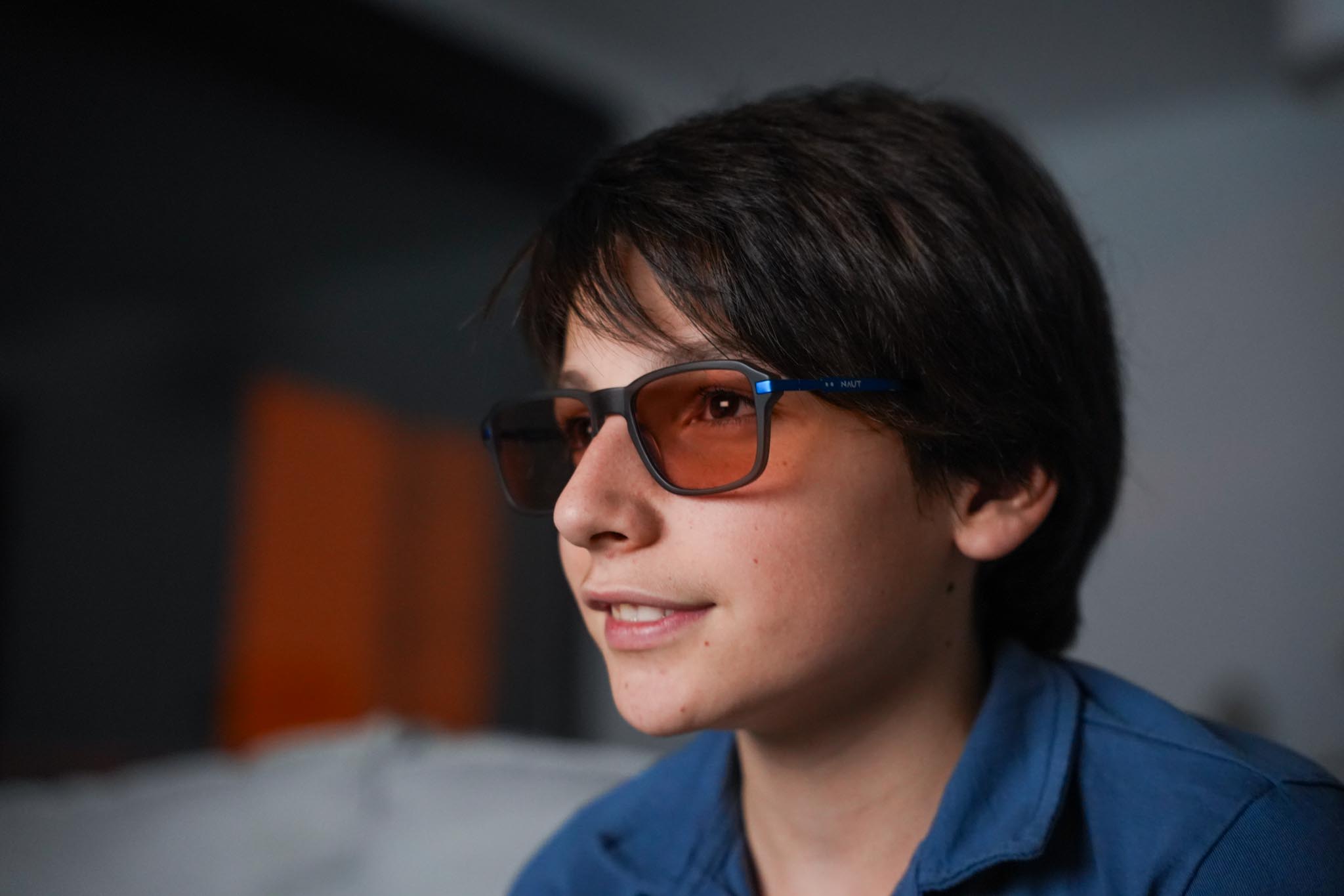 Man dressed in dark casual wear sitting alone in a stadium’s empty rows of purple chairs, lit by dramatic moody lighting.