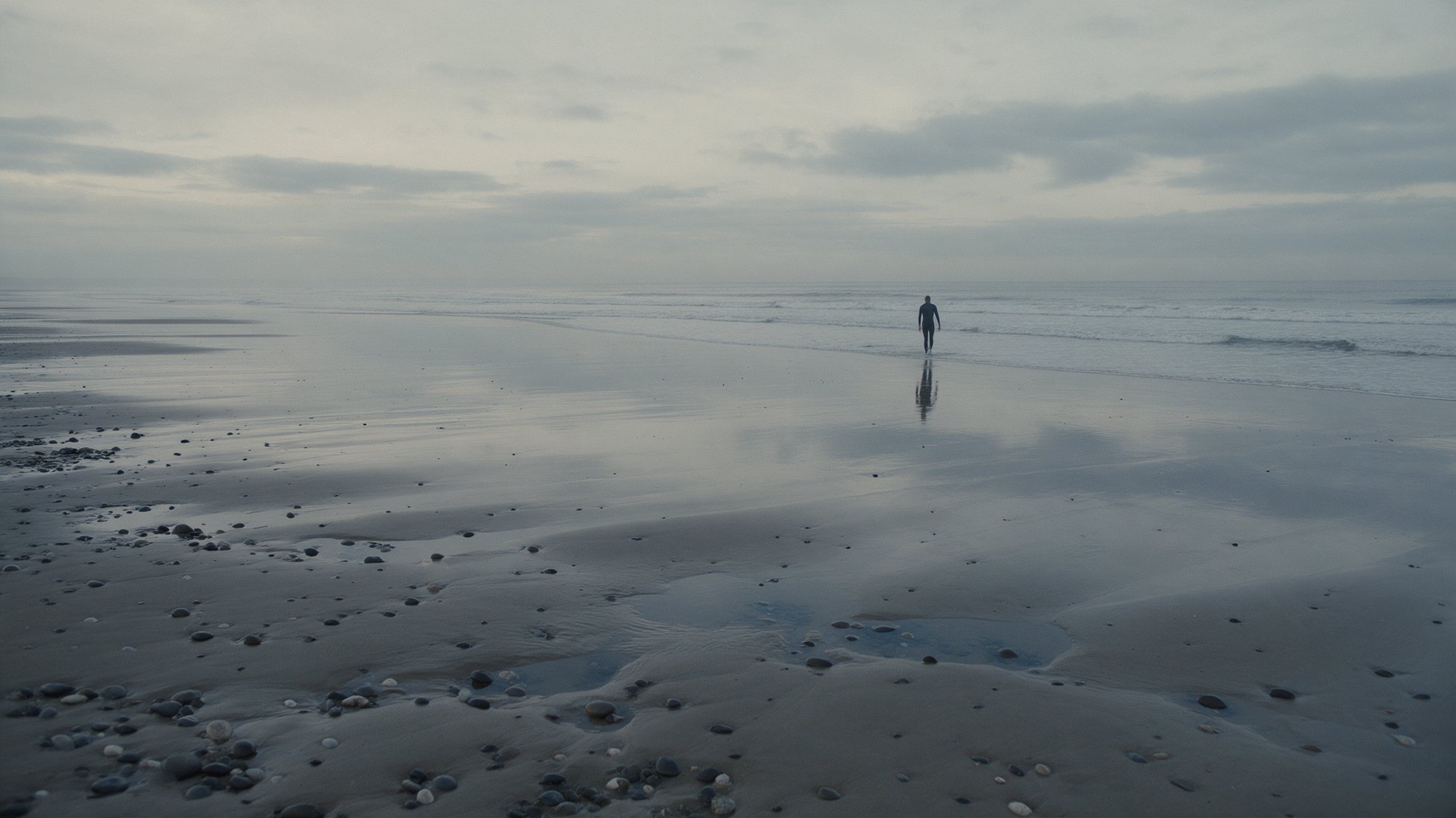 Lone figure walking toward the sea on a wide low-tide beach