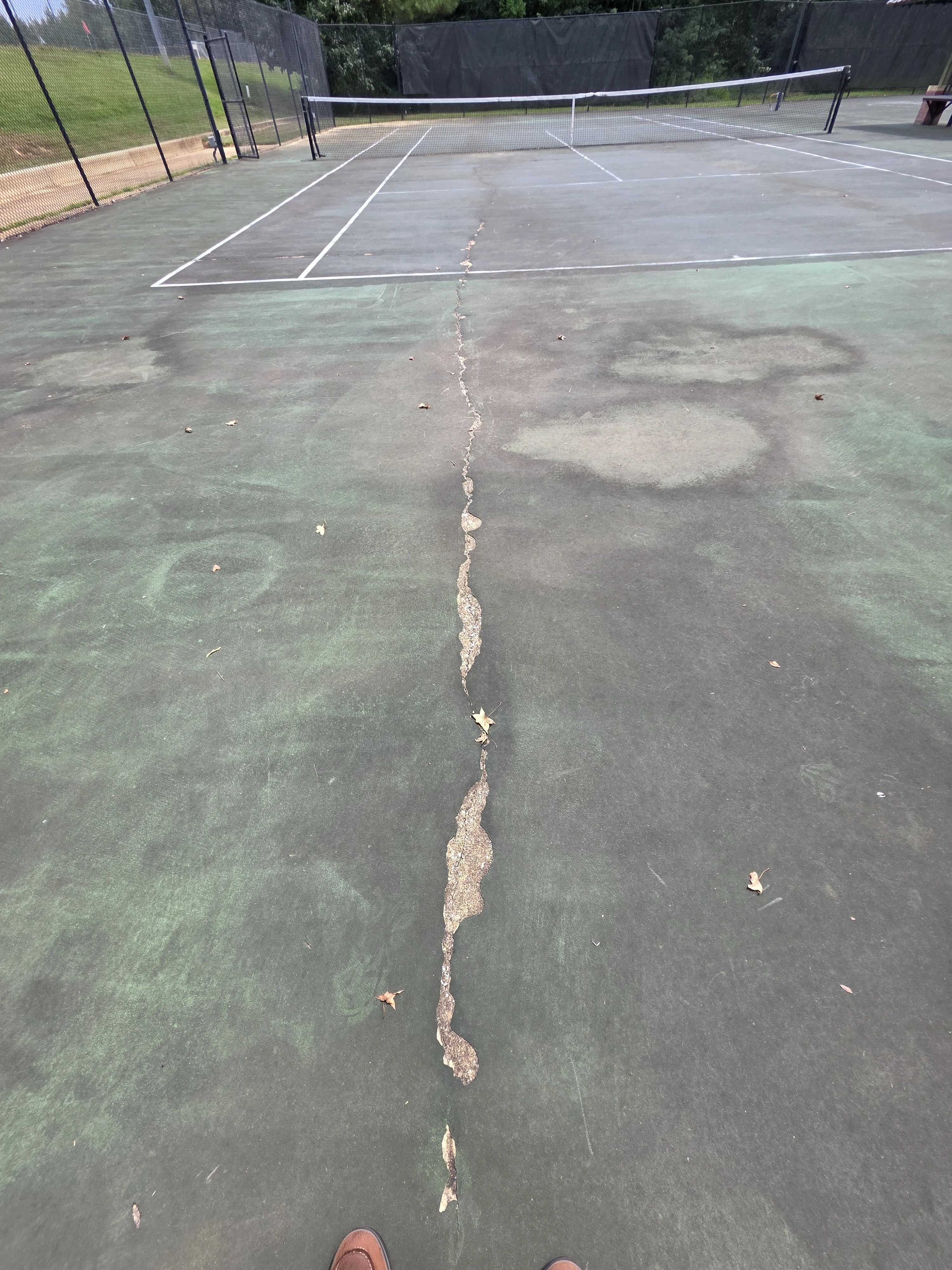 Long damaged crack running through worn tennis court surface before repairs in Corinth, MS