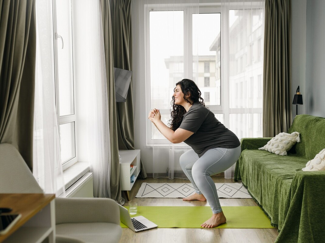 woman doing gym exercises to lose weight by performing squats in her living room while following an online exercise routine
