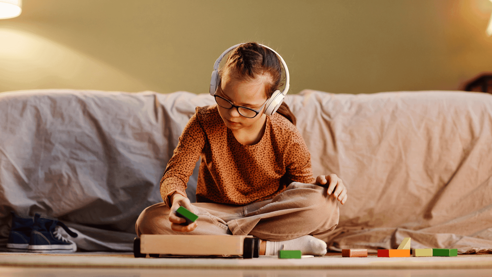 A young girl sitting on a sofa, wearing headphones and listening to HushAway®’s Sound Sanctuary while doing her homework.