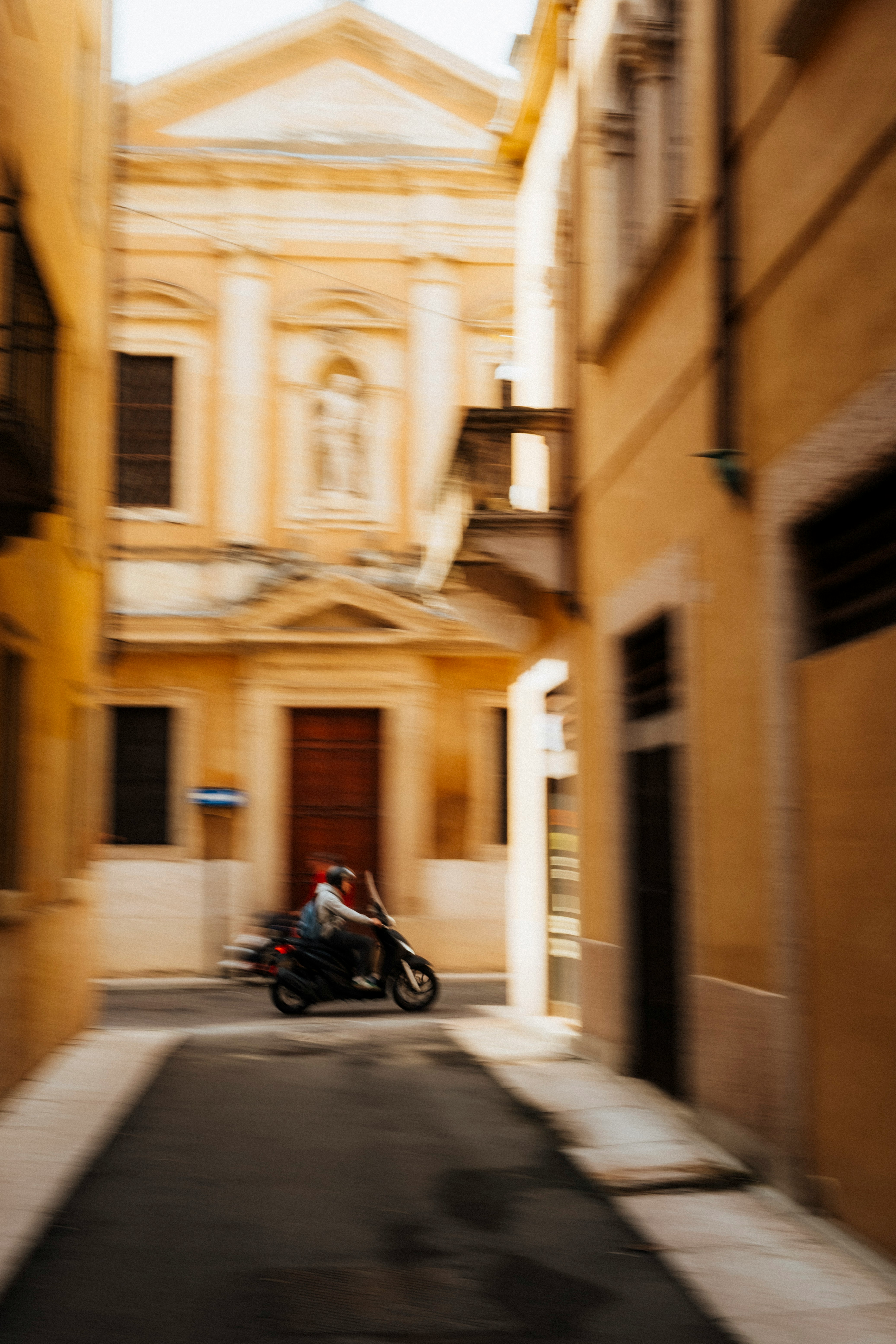 Motorcyclist rides down a narrow european street.