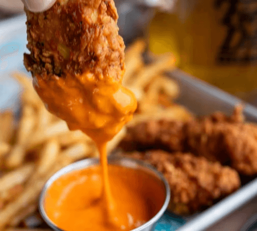 chicken fingers being dipped in buffalo sauce