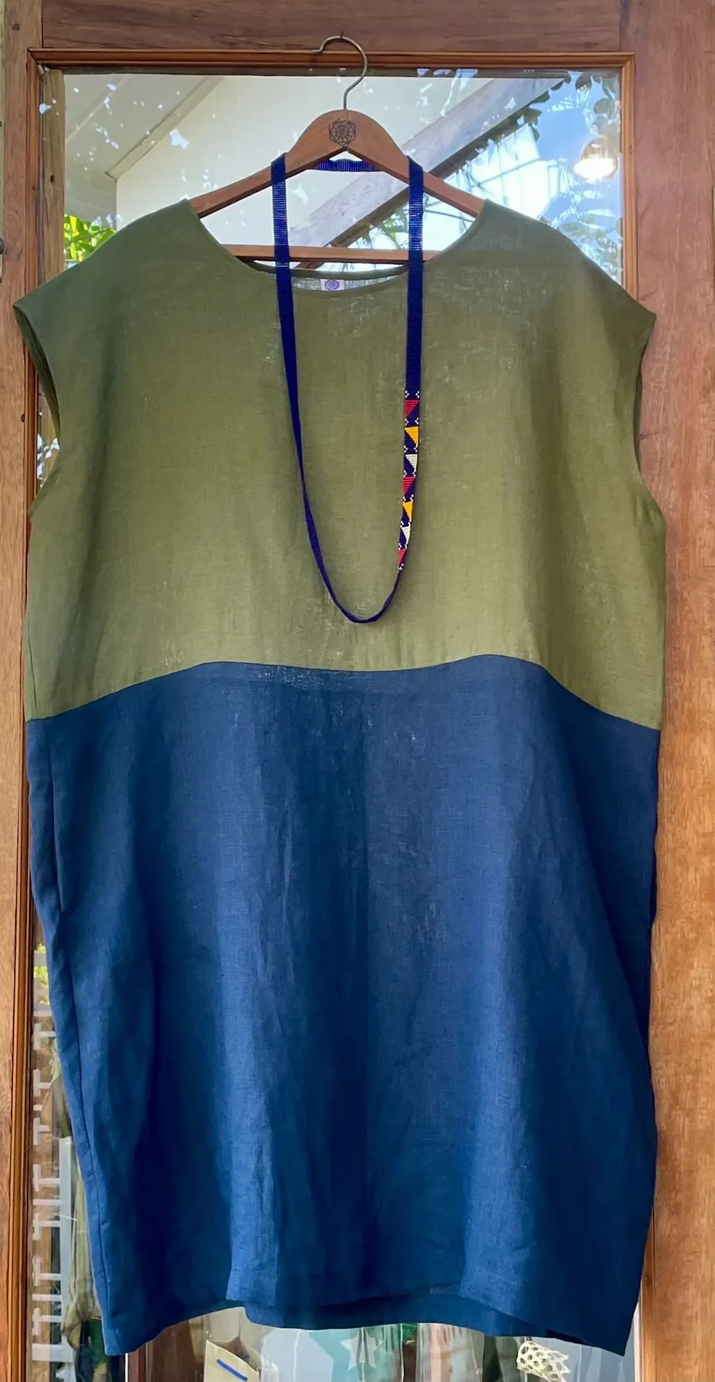Olive and indigo colour-block linen dress with a beaded necklace on a hanger at Jaali Boutique