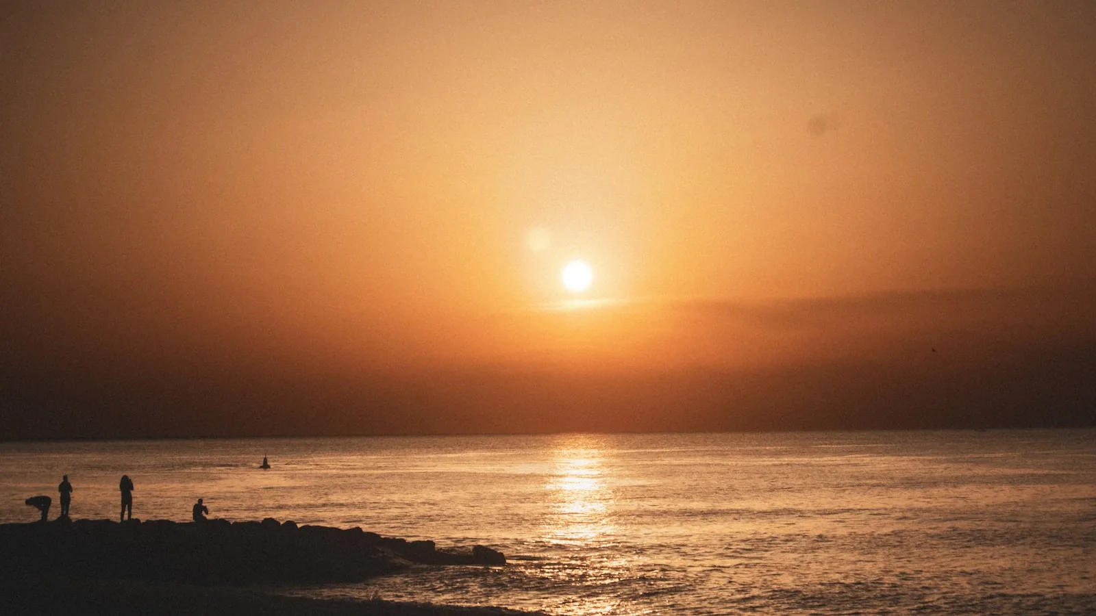 Sun setting over a calm sea, with people on the shoreline