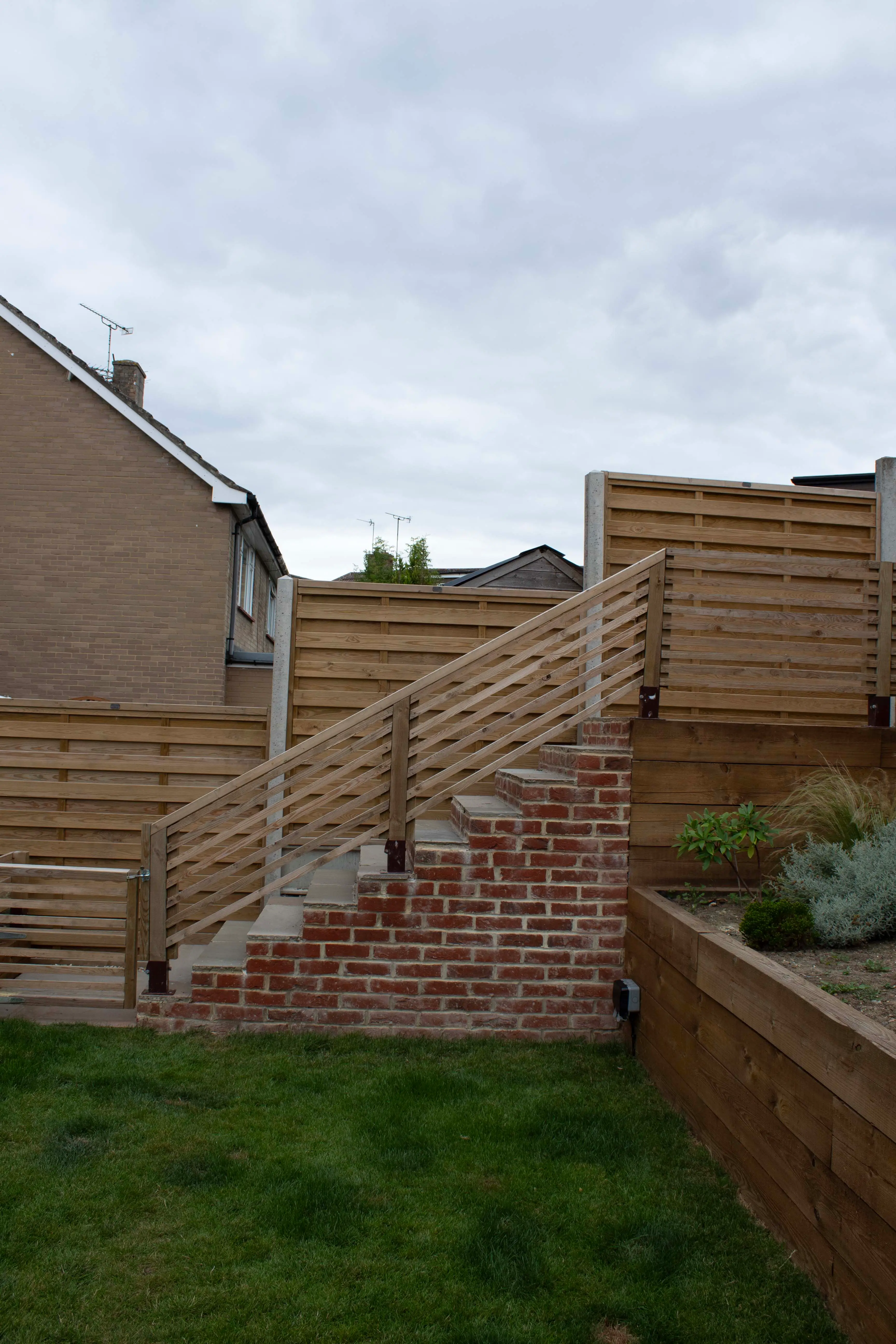 A view of a pathway leading between houses, with a grassy area and cloudy sky overhead.