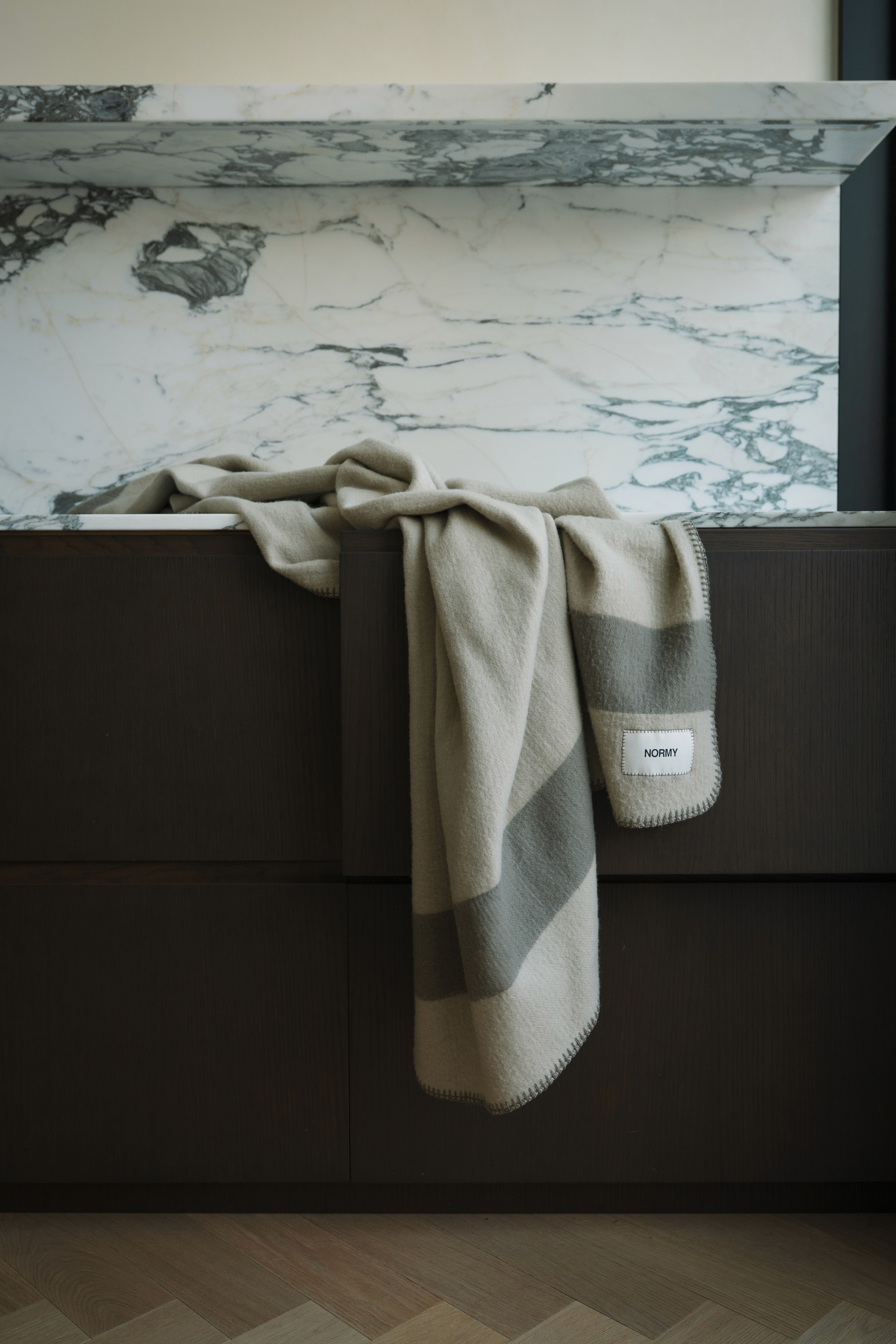 A pair of legs in bright blue socks rest on a soft, cream-colored NORMY blanket, emphasizing the blanket’s luxurious texture and signature branded tag.