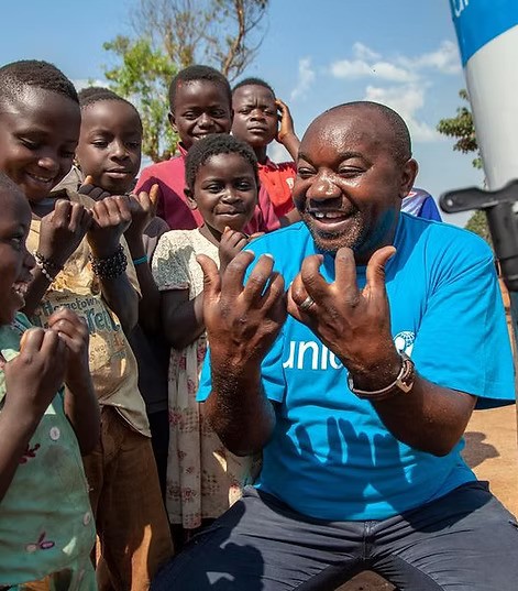 Ein lachender UNICEF-Mitarbeiter interagiert mit einer Gruppe von Kindern – Das soziale Engagement der DAG Unternehmensgruppe unterstützt lebenswichtige Hilfsprojekte und Bildung weltweit.
