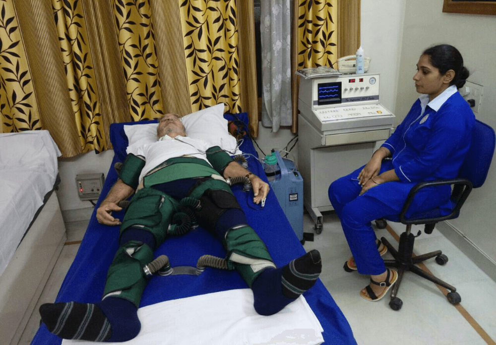 A patient undergoing EECP therapy at Sibia Medical Centre, lying on a treatment bed with inflatable cuffs around the legs and waist, connected to a computerized system for synchronized inflation and deflation. A healthcare professional monitors the procedure closely, ensuring comfort and effectiveness of the Enhanced External Counterpulsation therapy.