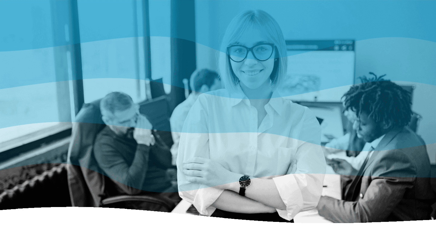 A confident professional wearing glasses and a white shirt stands in the foreground of a modern office, with three colleagues working collaboratively in the background, featuring large windows and a digital screen, embodying teamwork and productivity.