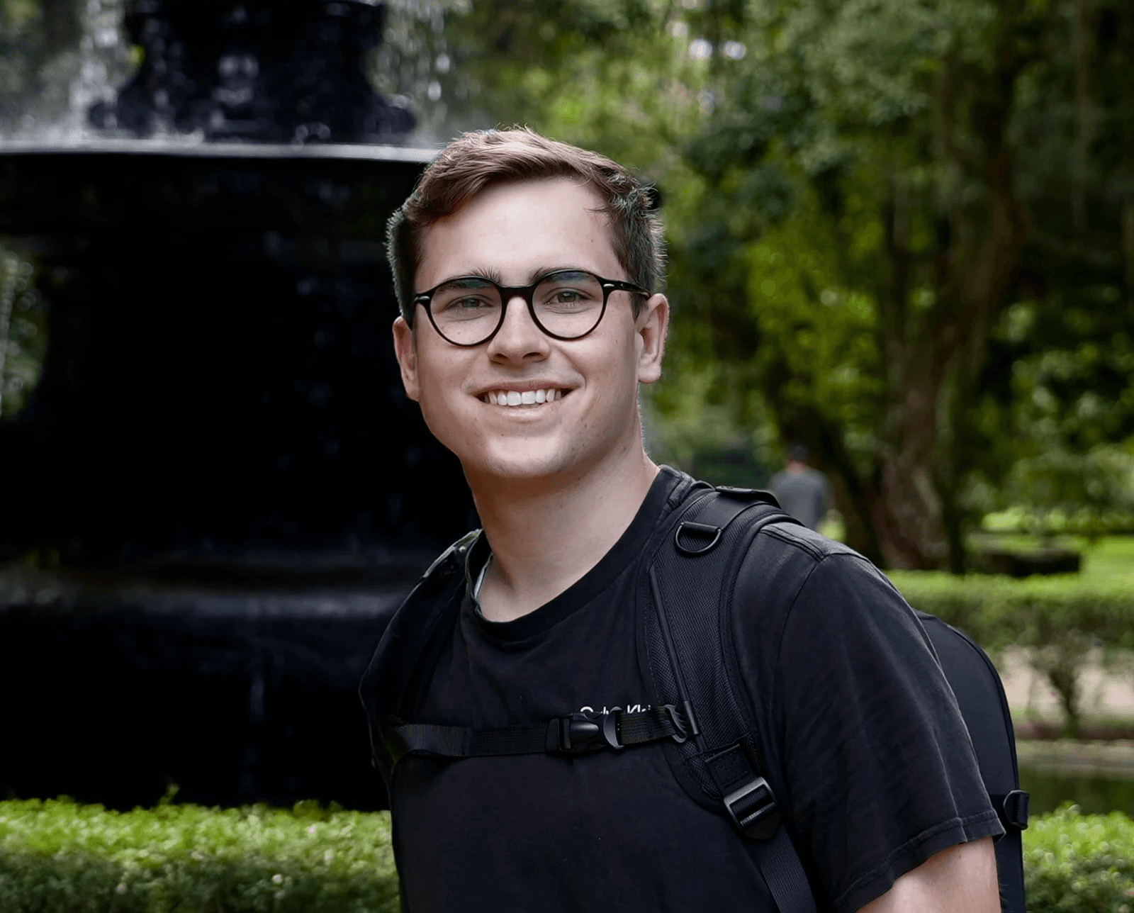 Photo of Erik Blankmeyer Jr., Founder of Bela Via with fountain and greenery in the background