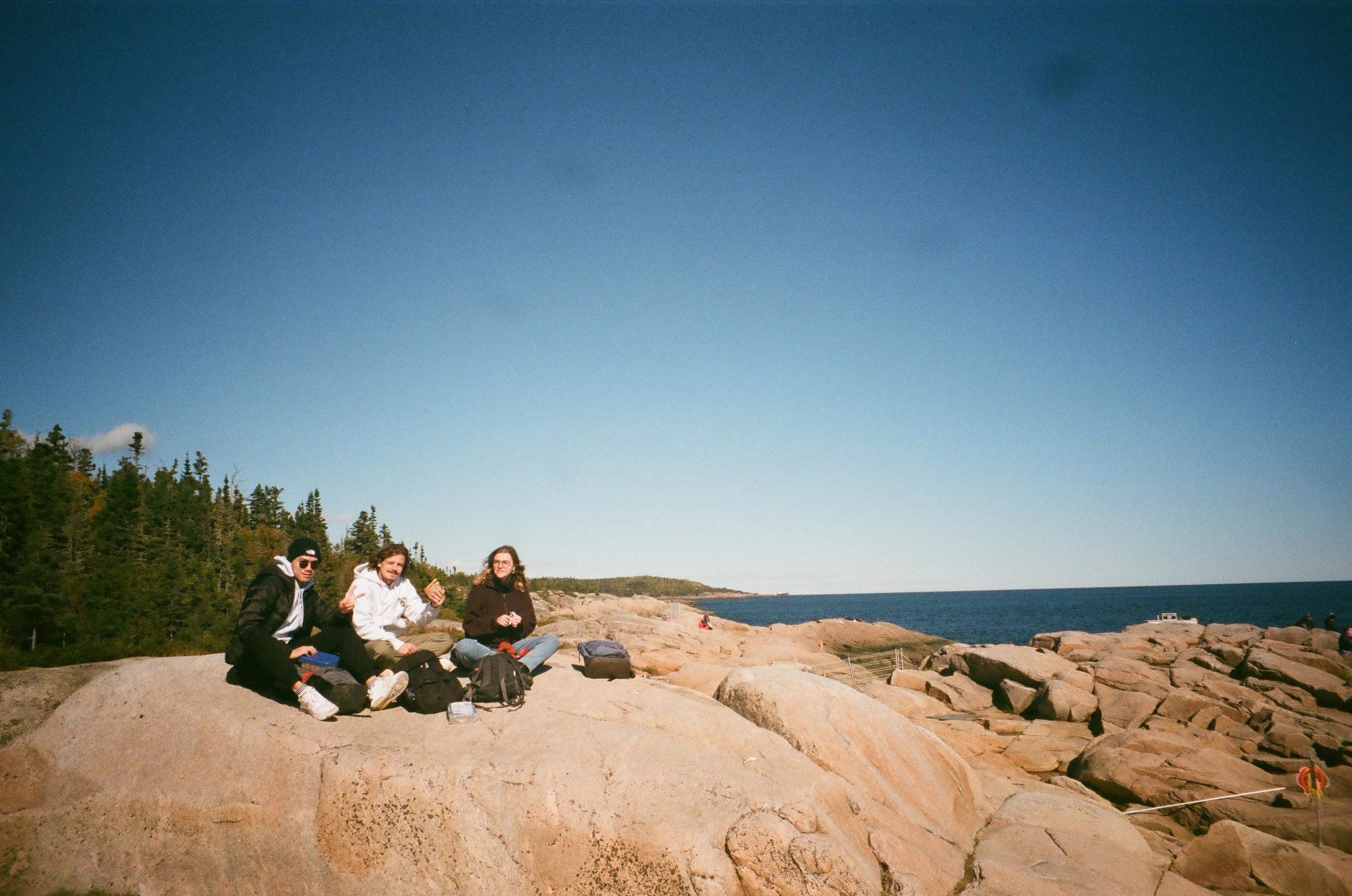 Trois amis assis sur des rochers du Cap de bon désir près du fleuve Saint-Laurent , profitant d'une journée ensoleillée.