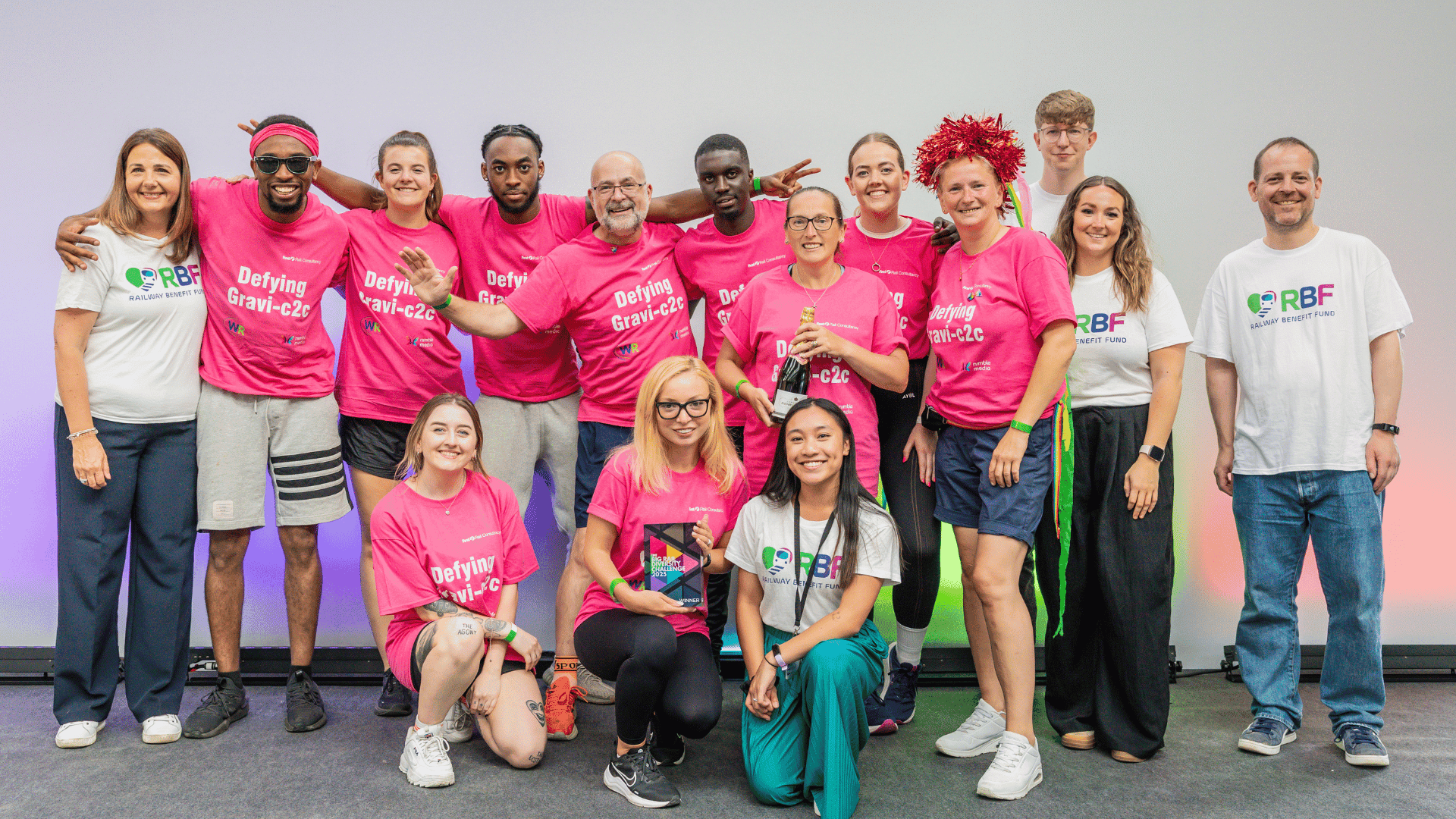 Outdoor team-building event with participants wearing matching blue shirts, taking part in inflatable obstacle courses and games, smiling and cheering, with the words 'ENTER A TEAM' in large bold white and green text across the image.