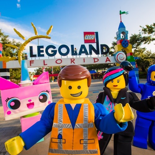 Group of Lego character mascots standing in front of the Legoland Florida entrance sign.