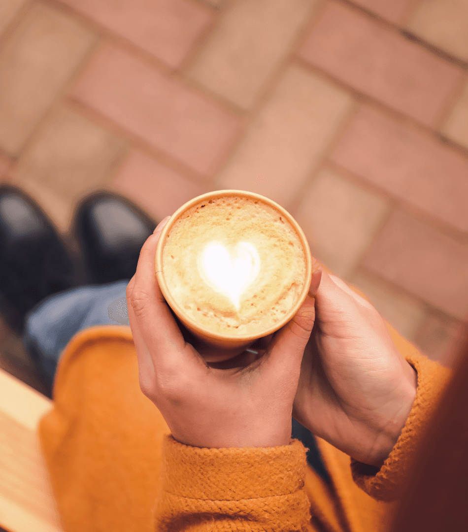 An overhead view of a user's hands holding an M&S takeaway coffee cup with a heart-shaped latte art design, highlighting the delightful user experience and a positive product detail.