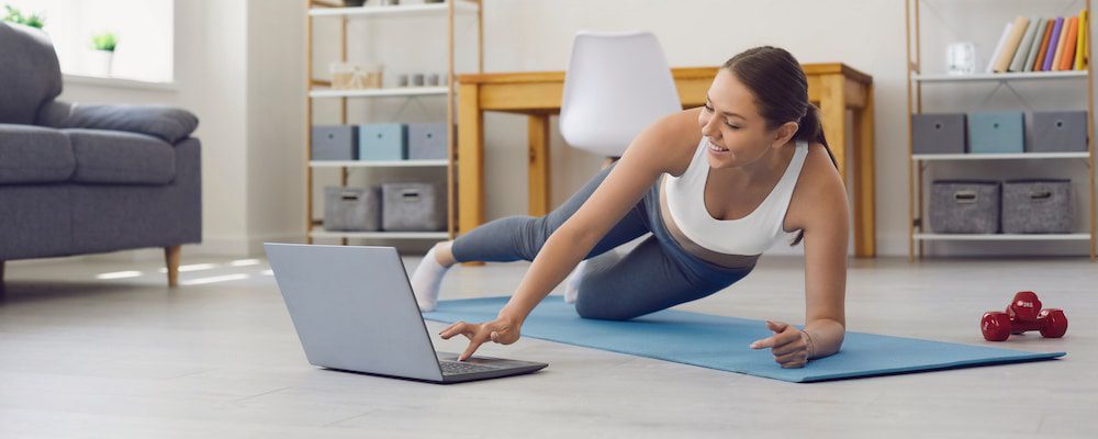 Woman doing side plank exercise while watching online workout on laptop in cozy home setting.