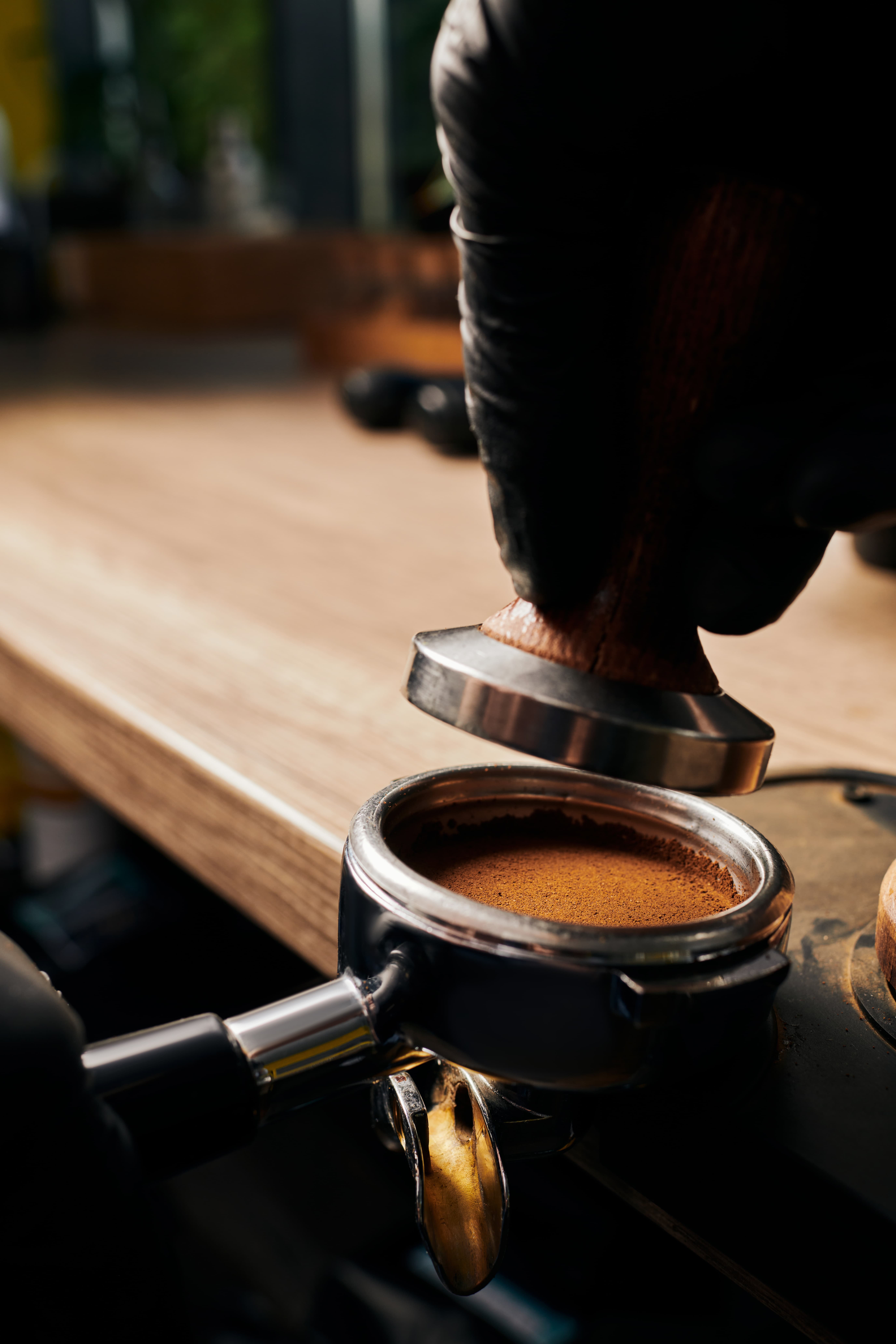 Close-up of a barista tamping espresso in a portafilter on a wooden counter, shot in a warm, moody style.