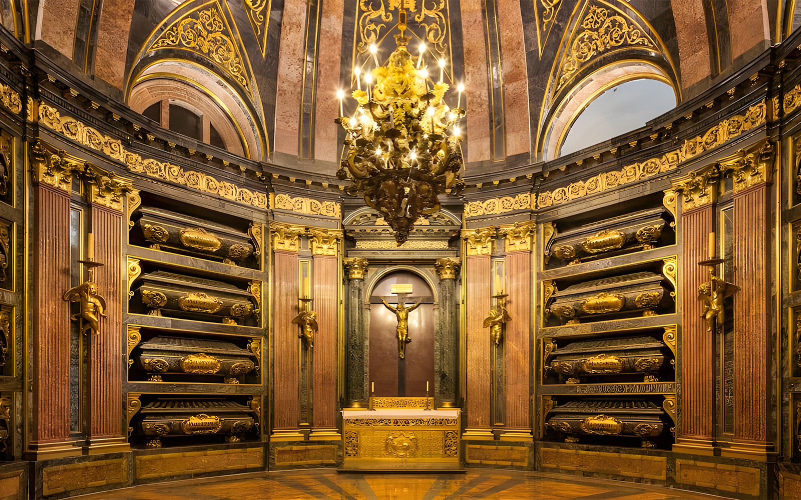 Inni í Konunglega Panteoninum í San Lorenzo de El Escorial, með skreyttum gullsmáatriðum og ljósakrónu.