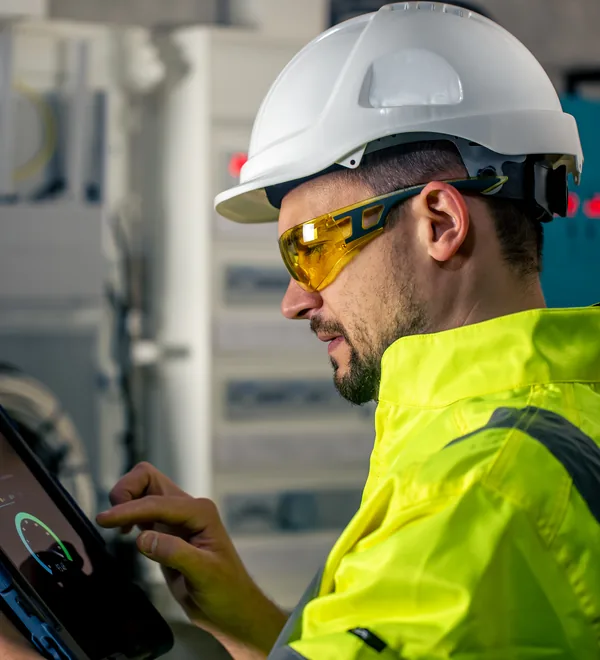 Technician in safety glasses using a tablet while working on an electrical control panel