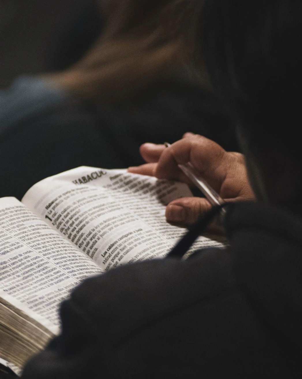 A speaker on stage, illuminated against a dark background, gestures while addressing an audience.