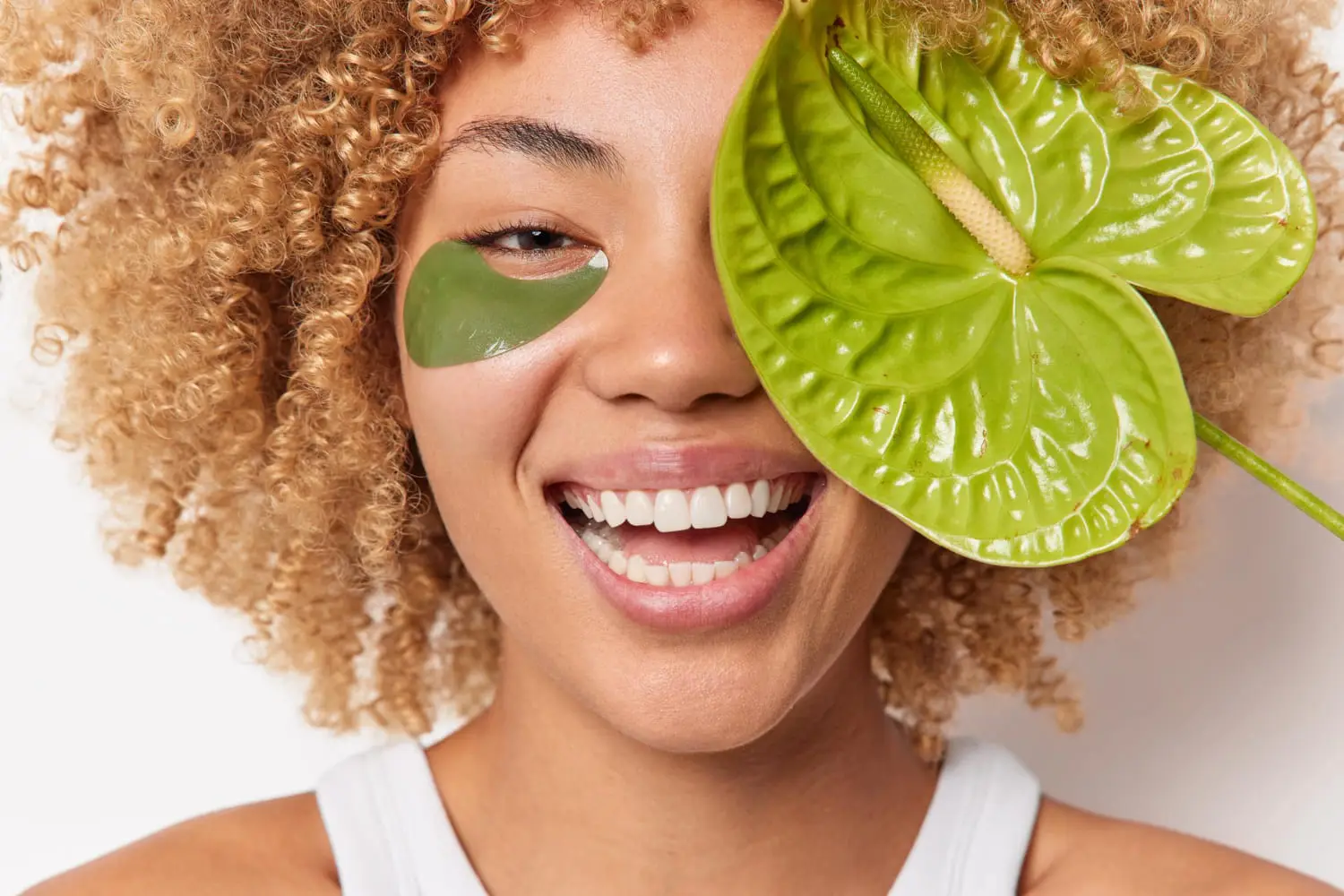 Smiling person with under-eye patch and green anthurium flower.