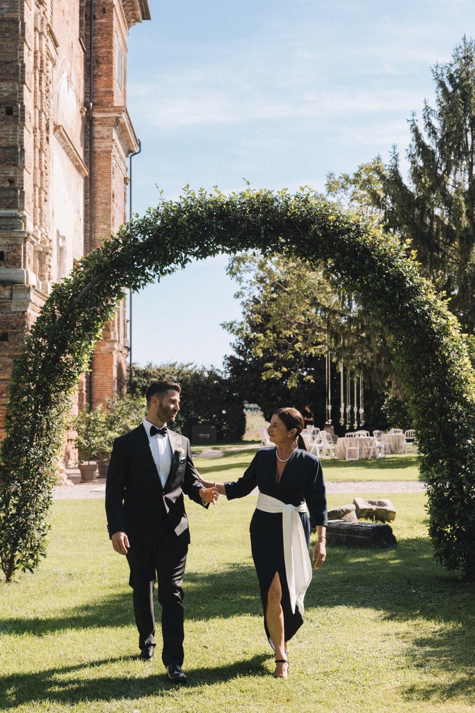 Sposi che camminano sotto arco floreale verde in giardino - matrimonio Rebecca e Giorgio a Villa La Favorita