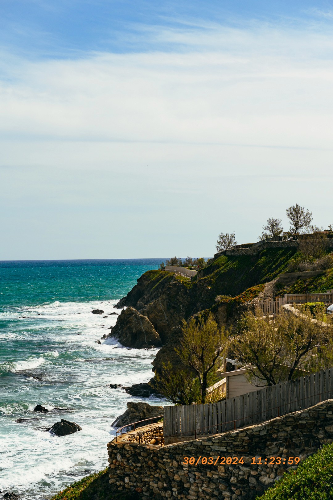 Côte rocheuse et mer turquoise, sentier en terrasse au-dessus des vagues.