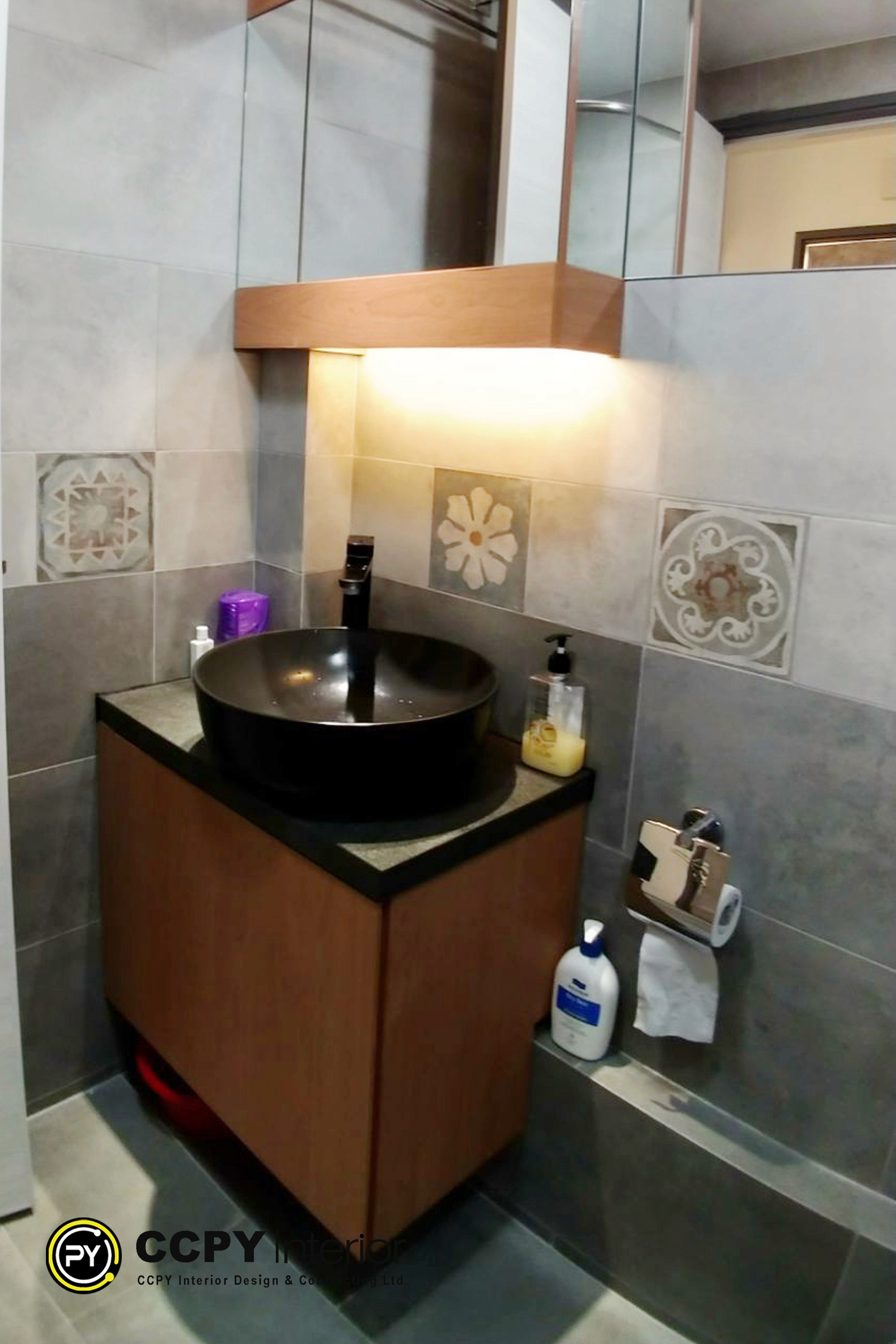 The selected region displays a bathroom vanity area that emphasizes tactile textures, patterned accent tiles, and distinct design features.Key Design FeaturesPatterned Accent Tiles: Square decorative tiles featuring geometric and floral motifs surround the vanity area.Vessel Sink: A dark, round basin sits prominently on top of the counter surface.Modern Fixtures: A sleek, matte black faucet coordinates with the contemporary styling.Floating Vanity: A wooden under-sink cabinet provides storage while maintaining open floor space underneath.Under-Cabinet Lighting: Hidden strip lighting beneath the vanity illuminates the floor and adds depth.